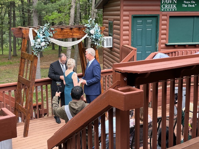 An outdoor wedding ceremony at a rustic cabin with a small group of guests.
